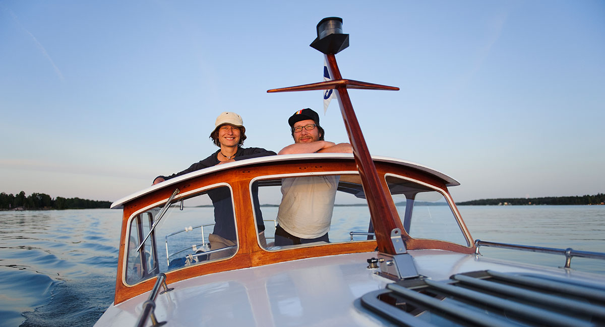 Två personer på medelstor motorbåt tittar leende in i kameran.
