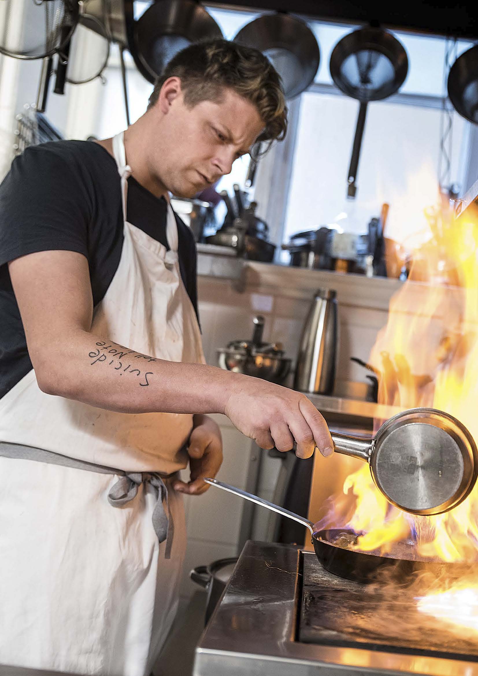 Joakim Almqvist befinner sig i restaurangköket och lagar mat. Från kastrullen stiger lågor när han flamberar något.