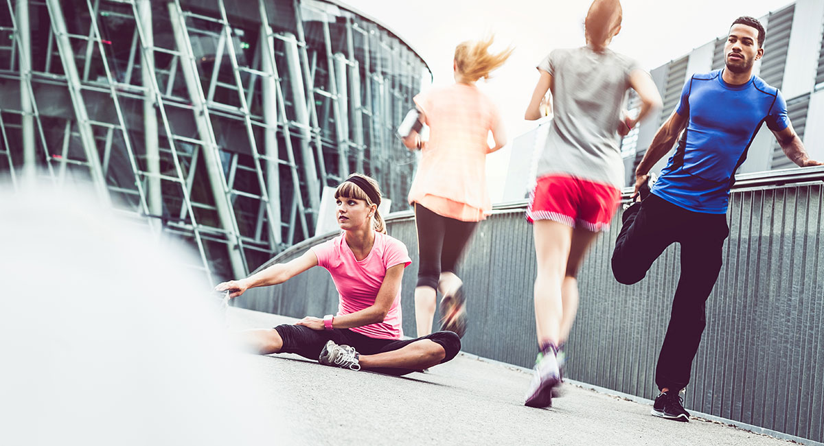 Fyra personer på en gångbro. Två kvinnor joggar bort från kameran, en man och en kvinna utför stretchövningar.