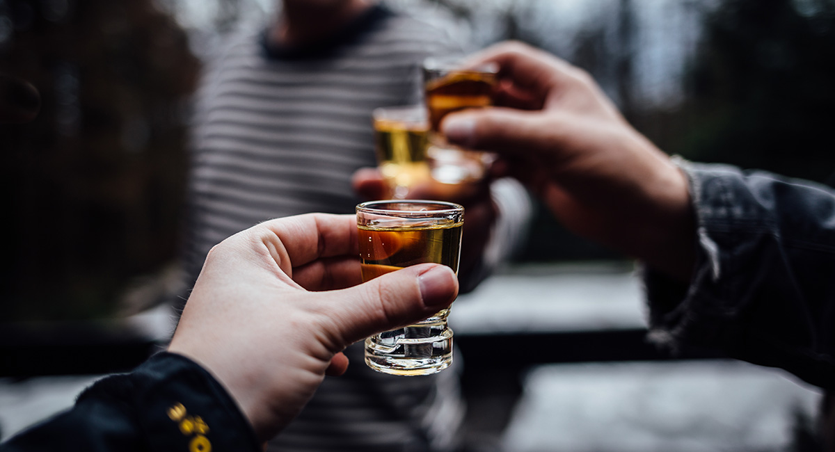 Närbild på tre händer som håller i varsitt shotglas och skålar med varandra