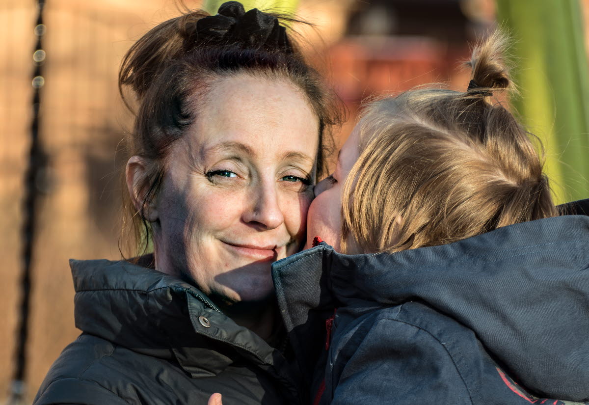 Närbild på Sofie som håller i sin son. Sonen pussar henne på kinden och Sofie ler