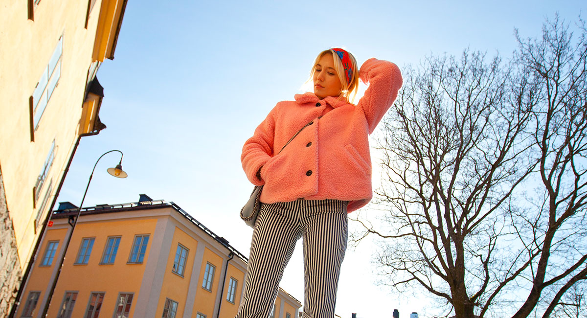 Josephine Dahlberg Bild tagen utomhus på Josephine Dahlberg vid lägenhetshus. Josephine har randiga byxor och det är blå himmel