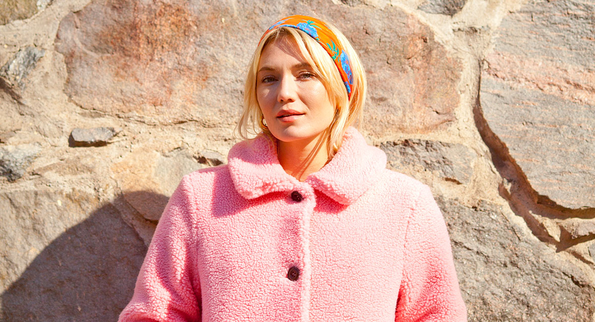 Josephine Dahlberg Porträttbild på Josephine Dahlberg. Josephine är blond, har en scarf i håret och står lutad mot en mur
