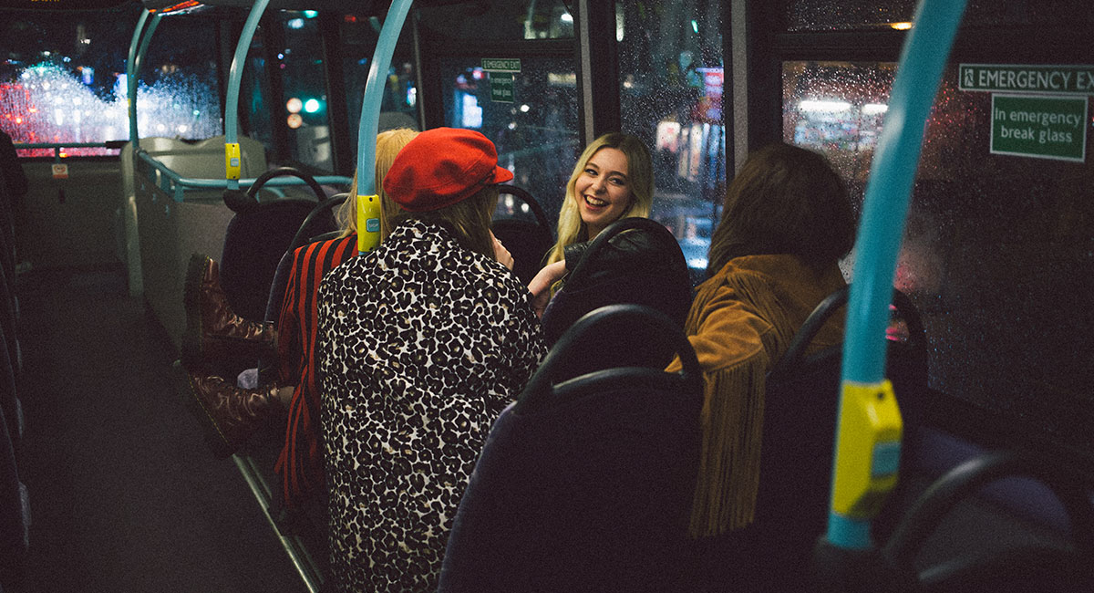Festande tonåringar på buss i stadsmiljö nattetid.