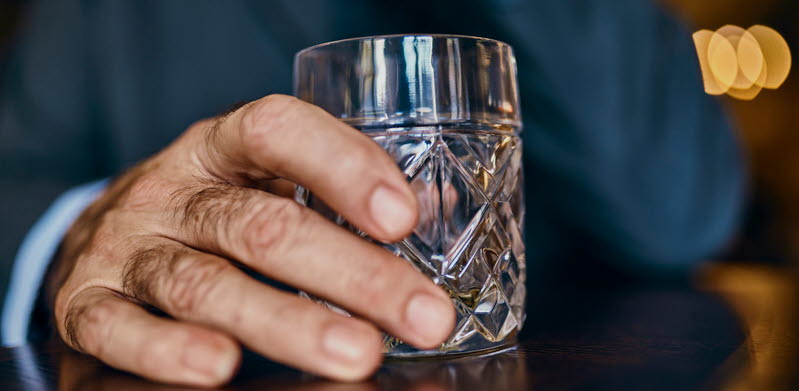 Närbild på en hand som håller i ett glas med whiskey i